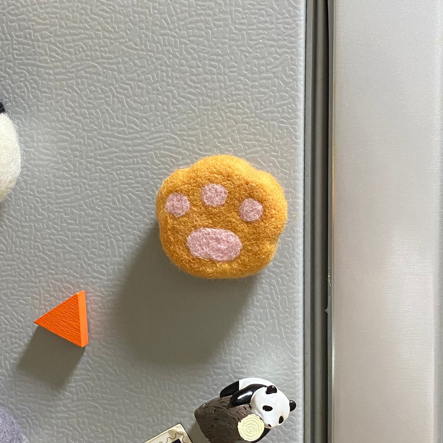 Handmade wool felt fridge magnet shaped like an orange tabby cat paw, adding a cozy, personal touch for cat lovers